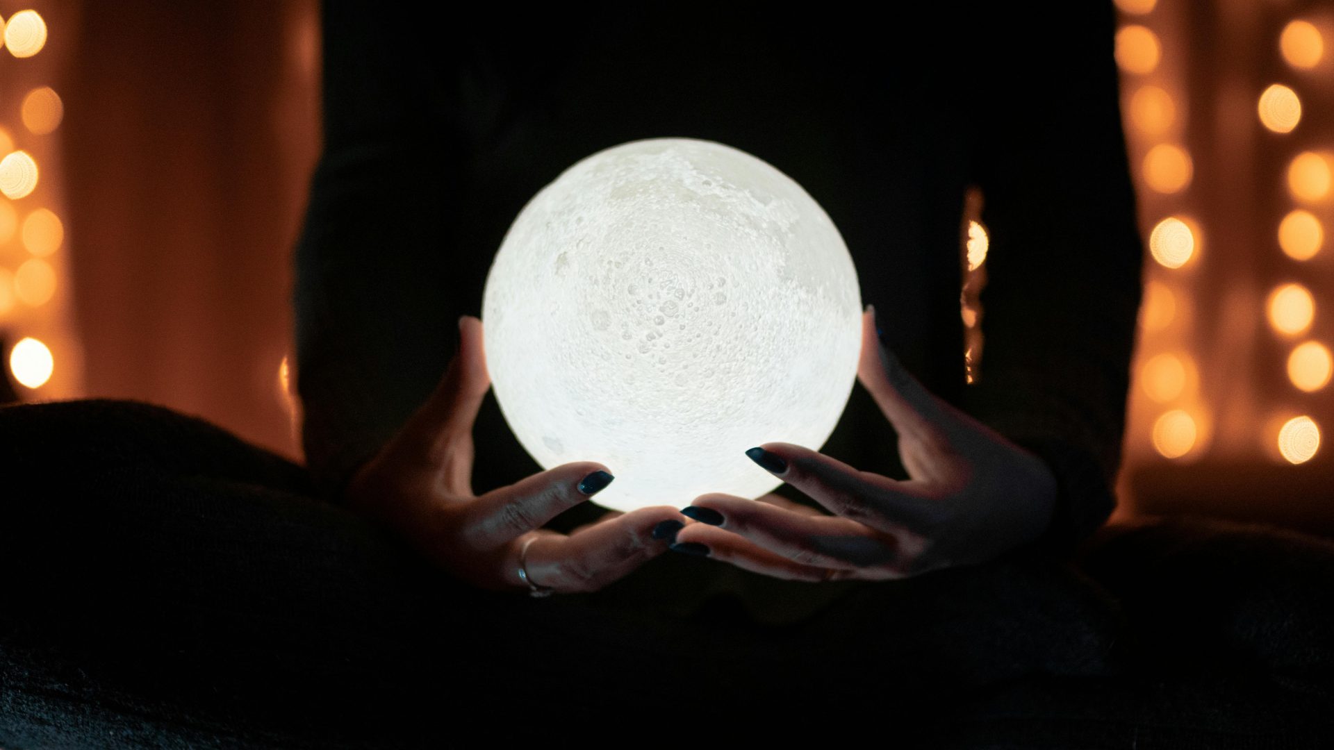 Une personne tenant une lampe lune scintillante, entourée de lumières bokeh chaudes, créant une atmosphère intérieure mystique.