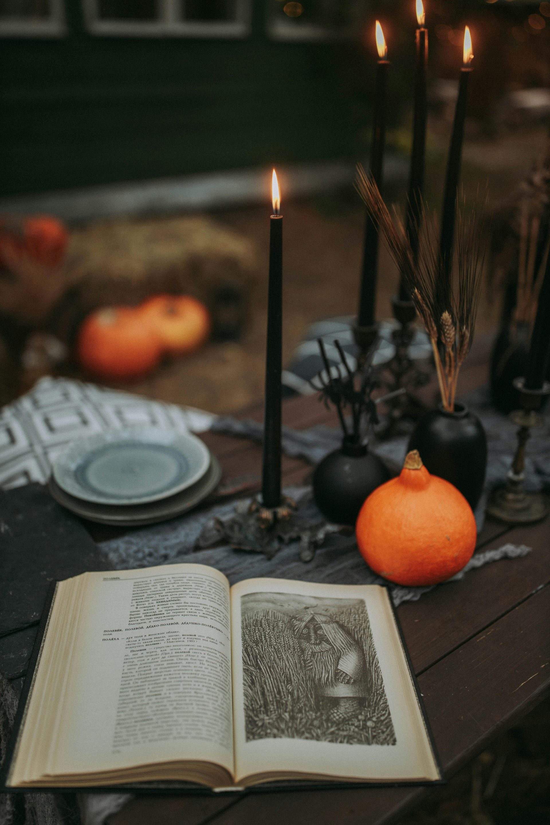 Une décoration sur le thème d'Halloween avec un livre ouvert, des bougies noires et des citrouilles sur une table rustique.